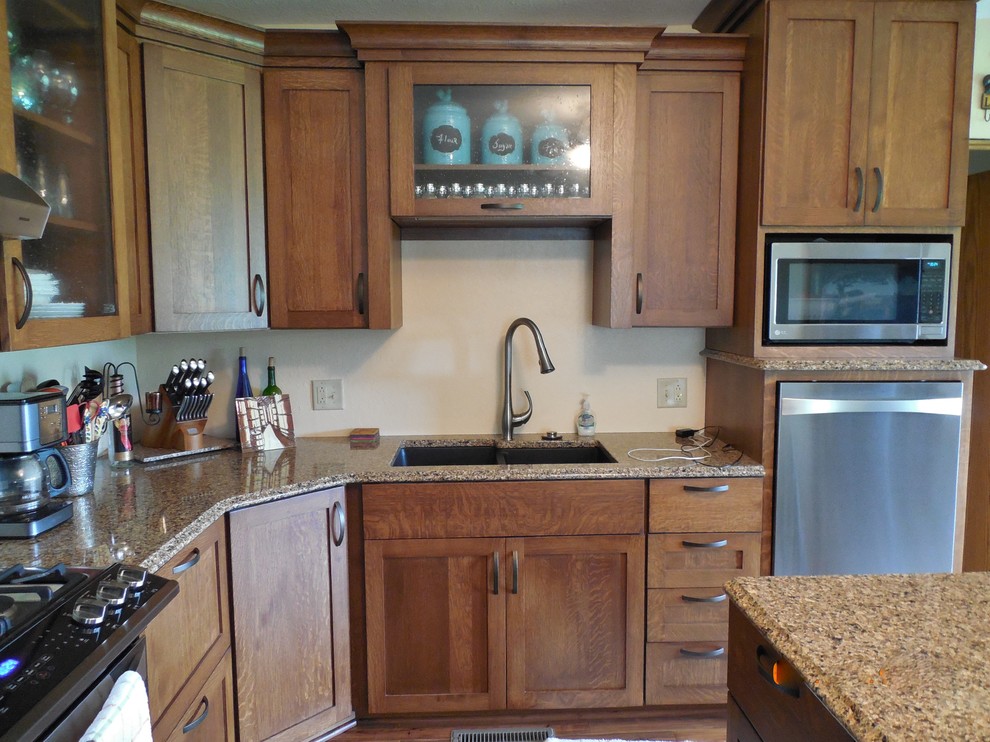 This is an example of a mid-sized country l-shaped eat-in kitchen in Cedar Rapids with an undermount sink, shaker cabinets, brown cabinets, stainless steel appliances, medium hardwood floors and with island.