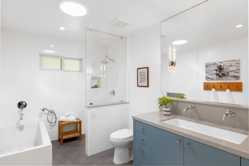 Large transitional kids bathroom in Other with flat-panel cabinets, blue cabinets, a freestanding tub, an open shower, a two-piece toilet, white tile, ceramic tile, white walls, ceramic floors, a drop-in sink, engineered quartz benchtops, grey floor, an open shower and grey benchtops.