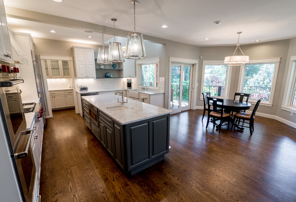 Example of a large transitional u-shaped medium tone wood floor and brown floor eat-in kitchen design in Portland with a farmhouse sink, raised-panel cabinets, gray cabinets, marble countertops, white backsplash, subway tile backsplash, stainless steel appliances and an island