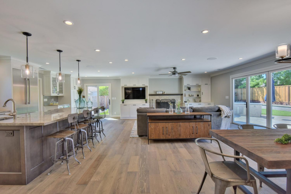 Mid-sized contemporary l-shaped open plan kitchen in San Francisco with an undermount sink, shaker cabinets, white cabinets, quartzite benchtops, grey splashback, glass tile splashback, stainless steel appliances, laminate floors, with island, brown floor and multi-coloured benchtop.