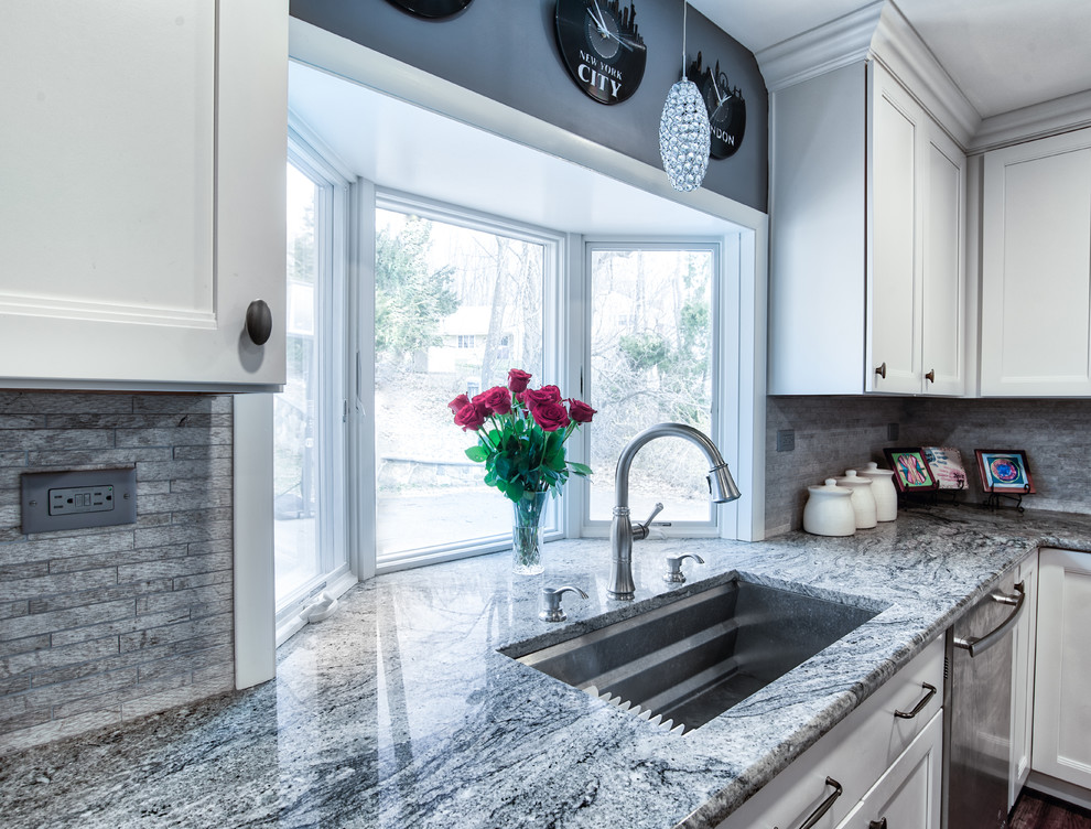 Mid-sized traditional l-shaped eat-in kitchen in New York with an undermount sink, shaker cabinets, white cabinets, grey splashback, stone tile splashback, stainless steel appliances, dark hardwood floors, with island and multi-coloured benchtop.