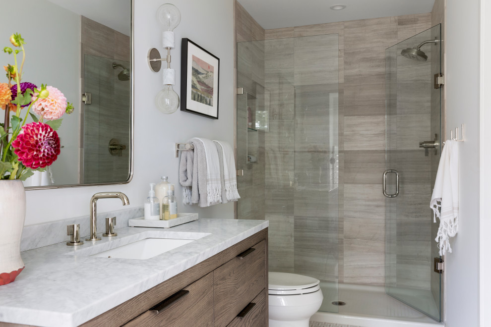 Design ideas for a transitional 3/4 bathroom in Minneapolis with flat-panel cabinets, medium wood cabinets, an alcove shower, a two-piece toilet, beige tile, travertine, white walls, mosaic tile floors, an undermount sink, marble benchtops, beige floor, a hinged shower door and white benchtops.
