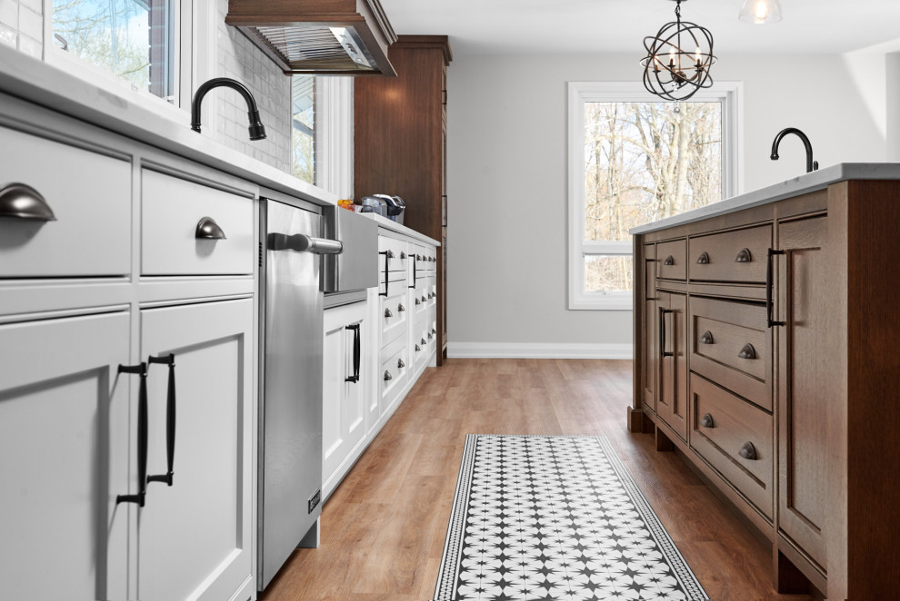 Enclosed kitchen - transitional galley light wood floor and brown floor enclosed kitchen idea in Toronto with a farmhouse sink, shaker cabinets, white cabinets, quartzite countertops, white backsplash, subway tile backsplash, stainless steel appliances, an island and white countertops