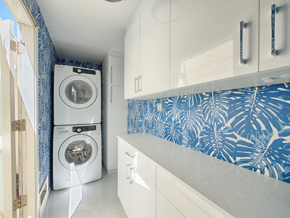 Idee per una piccola lavanderia minimalista con ante bianche, pareti blu, lavatrice e asciugatrice a colonna, pavimento grigio, top bianco e carta da parati