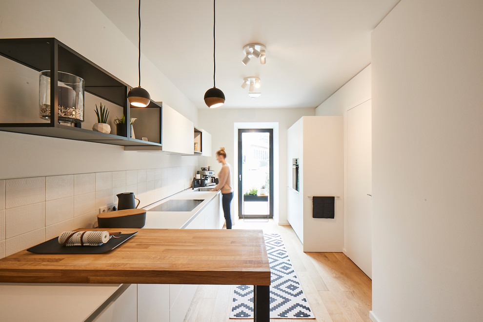 Inspiration for a mid-sized contemporary single-wall open plan kitchen in Hamburg with an integrated sink, flat-panel cabinets, white cabinets, white splashback, porcelain splashback, stainless steel appliances, light hardwood floors, no island, beige floor and white benchtop.