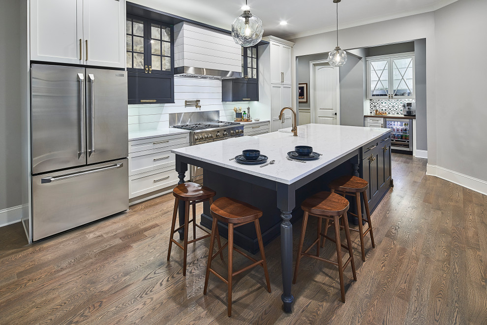 This is an example of a mid-sized transitional galley eat-in kitchen in Charlotte with a farmhouse sink, shaker cabinets, white cabinets, quartz benchtops, white splashback, shiplap splashback, stainless steel appliances, medium hardwood floors, with island, brown floor and white benchtop.