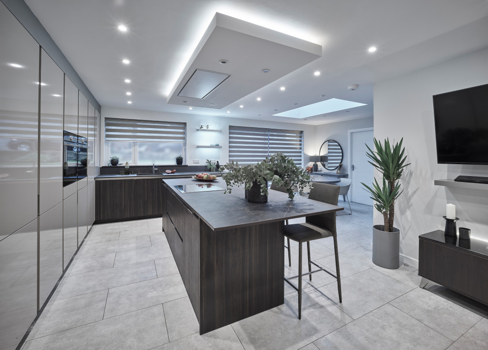 Large contemporary l-shaped eat-in kitchen in Other with dark wood cabinets, with island, black benchtop, an undermount sink, flat-panel cabinets, panelled appliances, porcelain floors and grey floor.