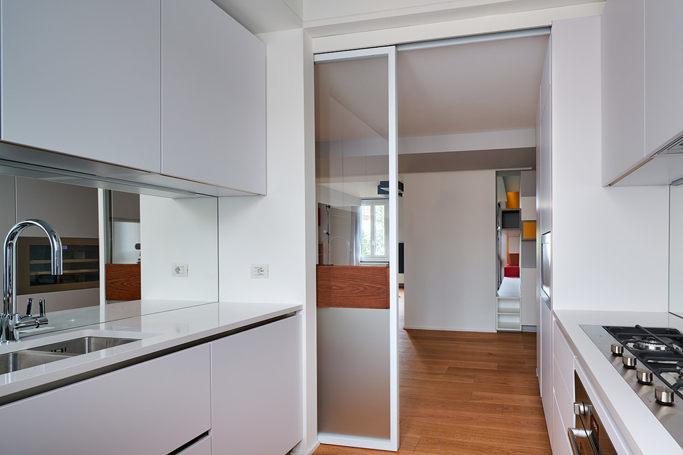 Mid-sized contemporary u-shaped separate kitchen in Milan with an undermount sink, flat-panel cabinets, white cabinets, quartz benchtops, stainless steel appliances and light hardwood floors.