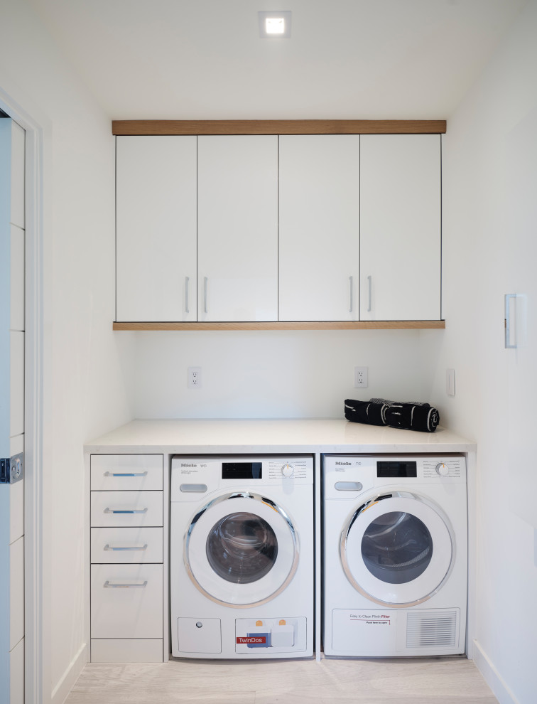 Mid-sized scandinavian single-wall dedicated laundry room in San Francisco with flat-panel cabinets, white cabinets, quartz benchtops, white splashback, white walls, light hardwood floors, a side-by-side washer and dryer and white benchtop.