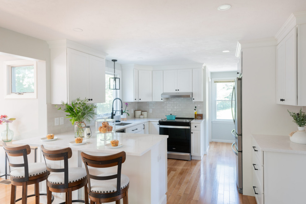 Example of a mid-sized transitional u-shaped medium tone wood floor and brown floor enclosed kitchen design in Boston with an undermount sink, shaker cabinets, white cabinets, quartz countertops, white backsplash, subway tile backsplash, stainless steel appliances, a peninsula and white countertops
