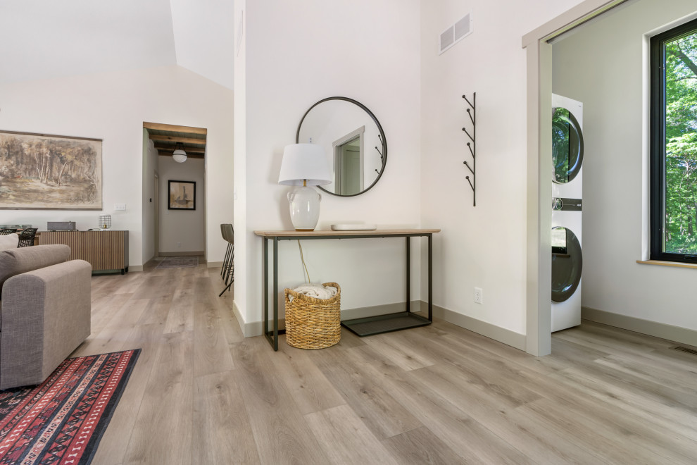 Ejemplo de cuarto de lavado abovedado actual pequeño con paredes blancas, suelo vinílico, lavadora y secadora apiladas y suelo marrón
