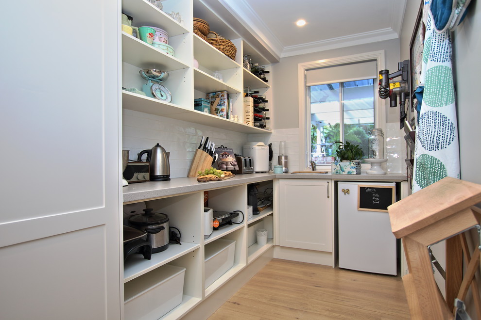 This is an example of a large eclectic l-shaped kitchen pantry in Sydney with an undermount sink, shaker cabinets, white cabinets, quartz benchtops, white splashback, subway tile splashback, stainless steel appliances, light hardwood floors, with island and brown floor.