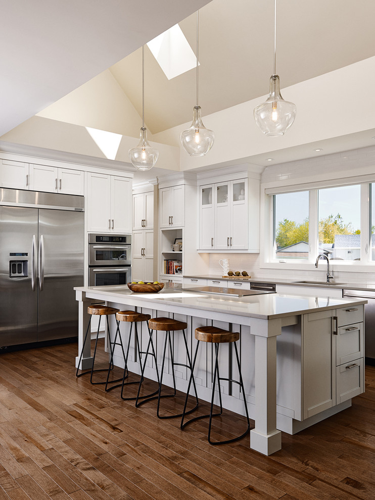 Example of a large transitional u-shaped medium tone wood floor open concept kitchen design with an undermount sink, shaker cabinets, white cabinets, quartz countertops, white backsplash, subway tile backsplash, stainless steel appliances and an island