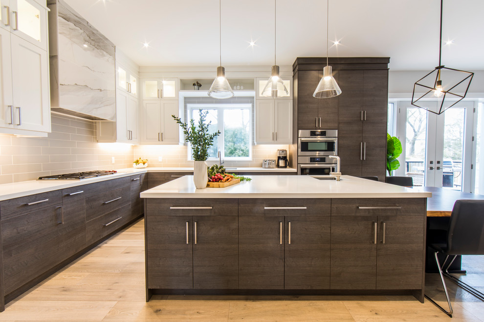Photo of a large contemporary l-shaped open plan kitchen in Toronto with an undermount sink, shaker cabinets, white cabinets, solid surface benchtops, grey splashback, subway tile splashback, stainless steel appliances, light hardwood floors, with island, beige floor and white benchtop.