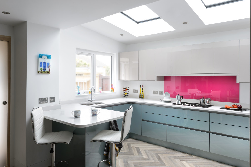 Inspiration for a medium sized contemporary u-shaped open plan kitchen in Cornwall with pink splashback, glass sheet splashback, light hardwood flooring, a submerged sink, flat-panel cabinets, grey cabinets, a breakfast bar, grey floors, white worktops and a vaulted ceiling.