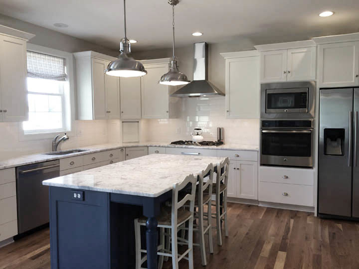 Photo of a mid-sized transitional l-shaped eat-in kitchen in DC Metro with an undermount sink, recessed-panel cabinets, white cabinets, marble benchtops, white splashback, ceramic splashback, stainless steel appliances, light hardwood floors and with island.
