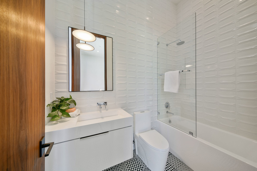 Inspiration for a mid-sized contemporary master bathroom in Los Angeles with flat-panel cabinets, white cabinets, a shower/bathtub combo, a one-piece toilet, white tile, white walls, a wall-mount sink, solid surface benchtops, multi-coloured floor, an open shower and white benchtops.