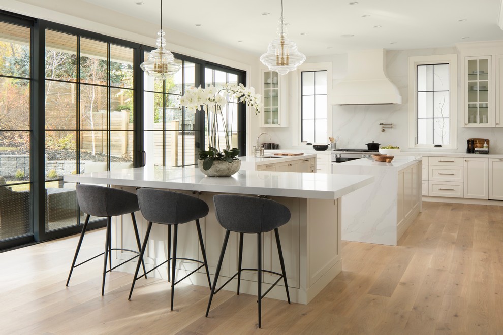 Transitional kitchen in Calgary with a double-bowl sink, recessed-panel cabinets, white cabinets, quartz benchtops, white splashback, panelled appliances, light hardwood floors, multiple islands and white benchtop.