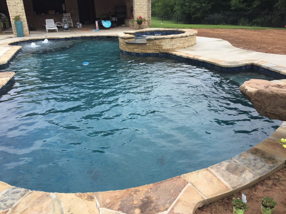 Photo of a tropical backyard custom-shaped natural pool in Oklahoma City with a hot tub.