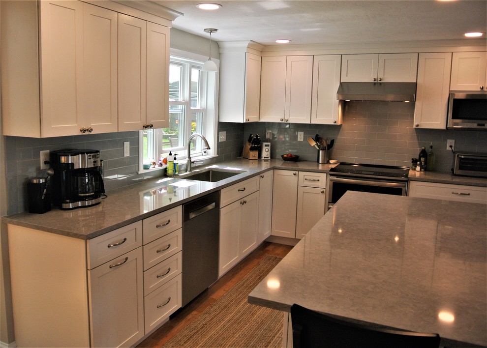 Kitchen - transitional light wood floor kitchen idea in Boston with an undermount sink, shaker cabinets, white cabinets, quartz countertops, gray backsplash, subway tile backsplash, stainless steel appliances, an island and gray countertops