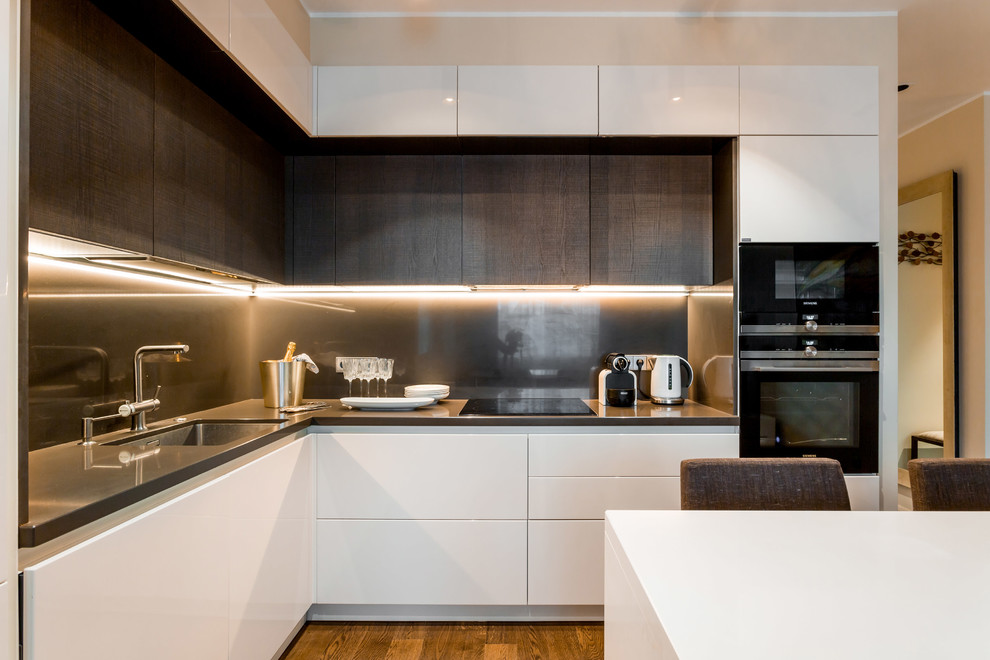 Medium sized l-shaped open plan kitchen in Moscow with a submerged sink, flat-panel cabinets, white cabinets, composite countertops, brown splashback, stone slab splashback, black appliances, medium hardwood flooring and an island.
