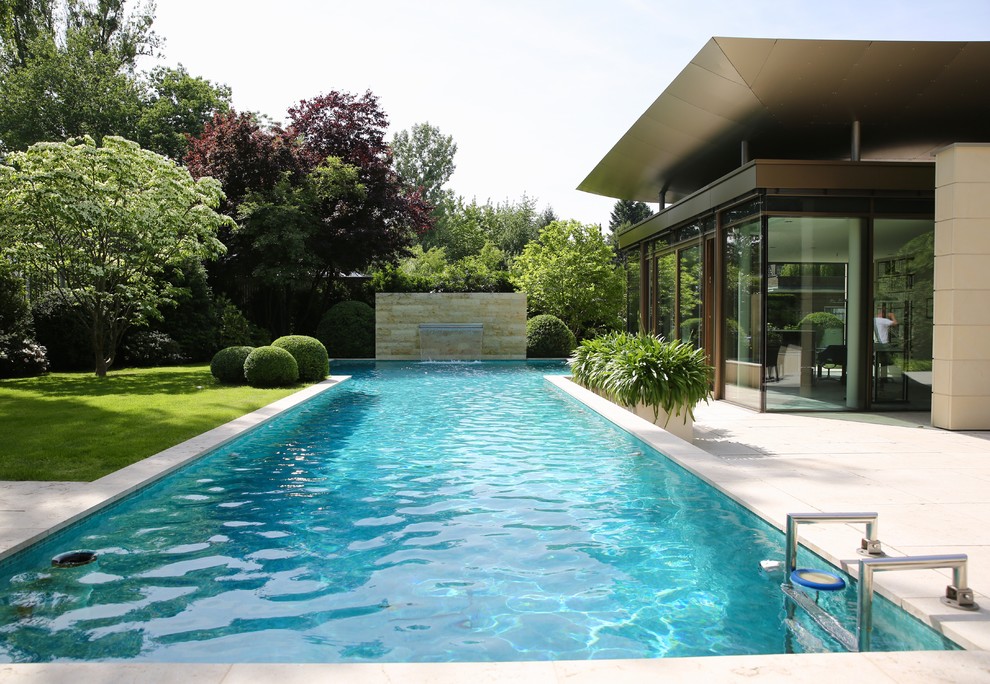 This is an example of a large contemporary backyard custom-shaped lap pool in Frankfurt with a water feature and tile.