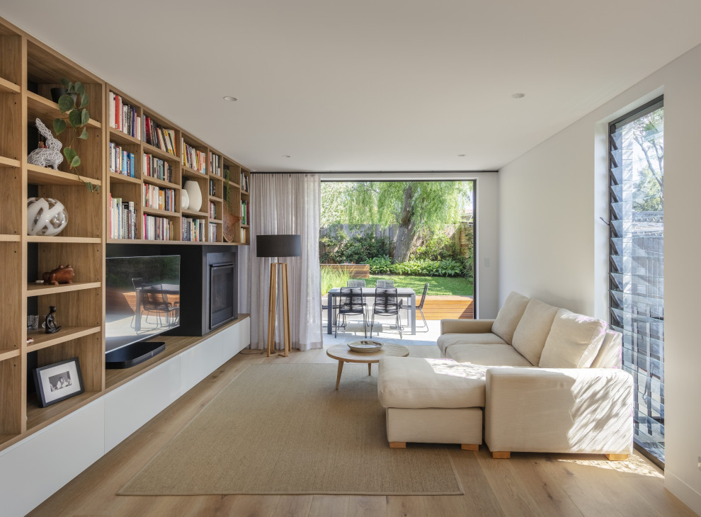 This is an example of a contemporary living room in Sydney with white walls, light hardwood floors, a standard fireplace, a built-in media wall and beige floor.