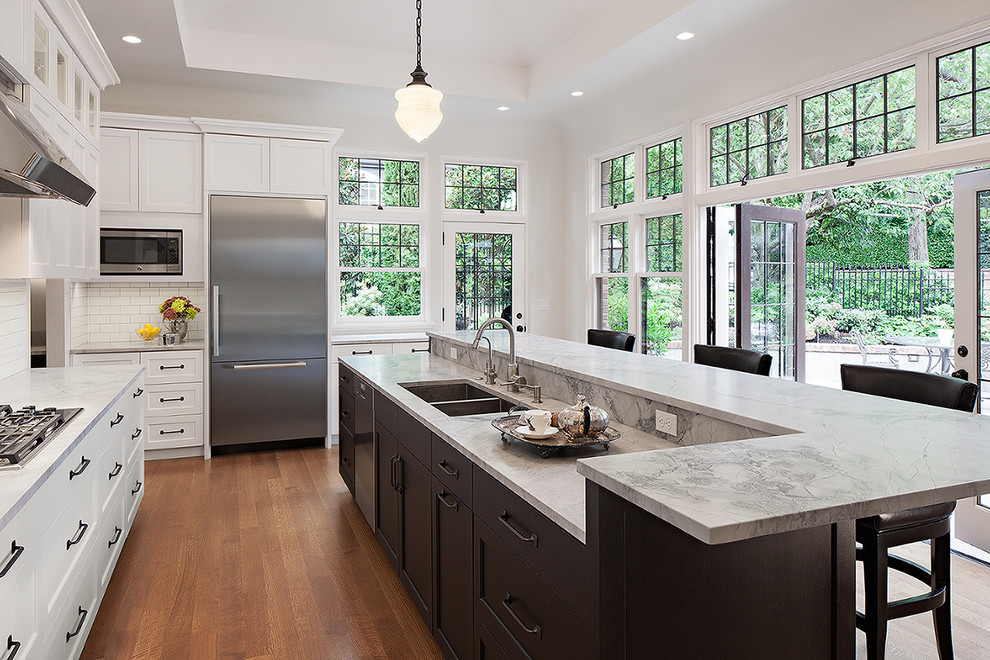 Design ideas for a mid-sized traditional u-shaped kitchen in Seattle with an undermount sink, flat-panel cabinets, white cabinets, quartzite benchtops, white splashback, subway tile splashback, stainless steel appliances, light hardwood floors and with island.