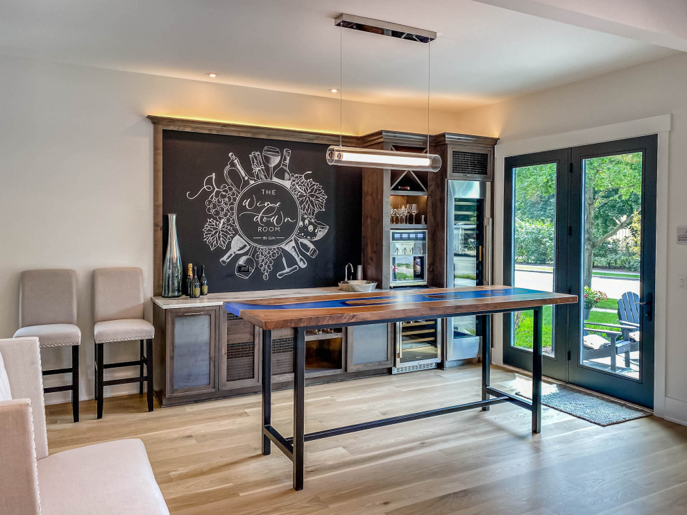 This is an example of a large contemporary single-wall wet bar in Chicago with an integrated sink, shaker cabinets, distressed cabinets, quartzite benchtops, black splashback, light hardwood floors and white benchtop.