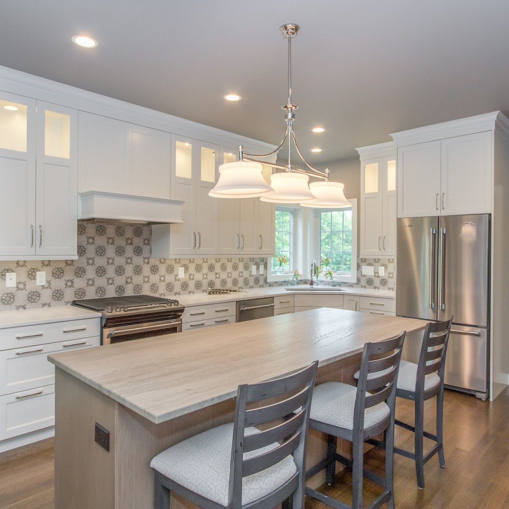 Example of a mid-sized transitional l-shaped medium tone wood floor and brown floor eat-in kitchen design in Cedar Rapids with a double-bowl sink, recessed-panel cabinets, white cabinets, quartz countertops, multicolored backsplash, porcelain backsplash, stainless steel appliances, an island and white countertops