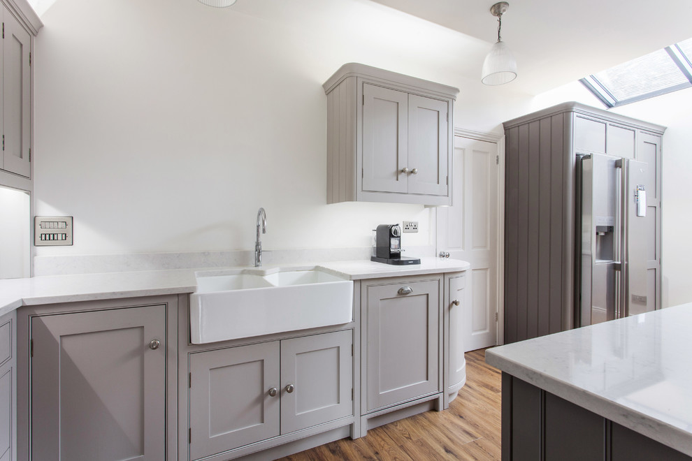 Photo of a large traditional l-shaped eat-in kitchen in Kent with a farmhouse sink, beaded inset cabinets, grey cabinets, quartzite benchtops, white splashback, subway tile splashback, black appliances, painted wood floors, with island and brown floor.