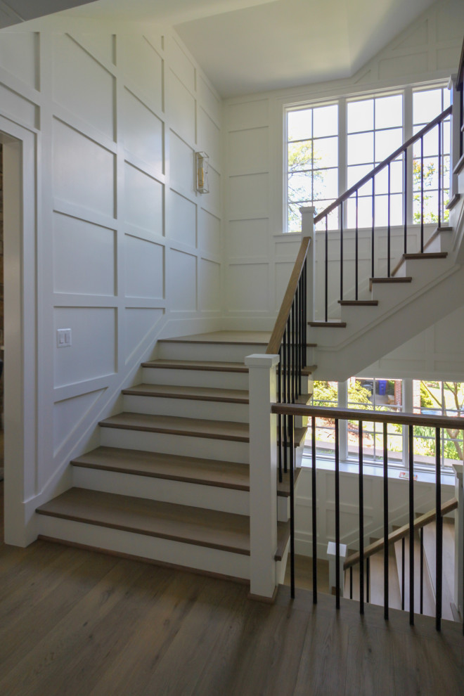 Свежая идея для дизайна: большая п-образная деревянная лестница в стиле неоклассика (современная классика) с деревянными ступенями, деревянными перилами и панелями на стенах - отличное фото интерьера