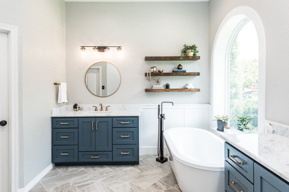 Photo of a large traditional master bathroom in Dallas with shaker cabinets, blue cabinets, a freestanding tub, an alcove shower, white tile, ceramic tile, grey walls, porcelain floors, an undermount sink, marble benchtops, multi-coloured floor, a sliding shower screen and white benchtops.