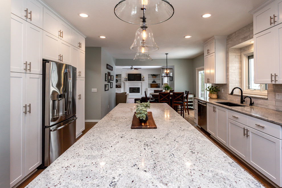 Example of a large transitional u-shaped medium tone wood floor and brown floor eat-in kitchen design with an undermount sink, recessed-panel cabinets, white cabinets, granite countertops, white backsplash, subway tile backsplash, stainless steel appliances, an island and gray countertops