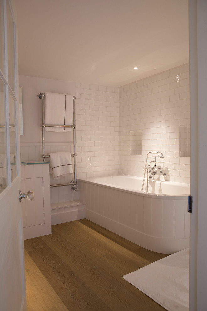 Photo of a mid-sized traditional kids bathroom in Oxfordshire with a drop-in tub, a shower/bathtub combo, a one-piece toilet, white tile, stone tile, white walls, light hardwood floors, a drop-in sink and an open shower.