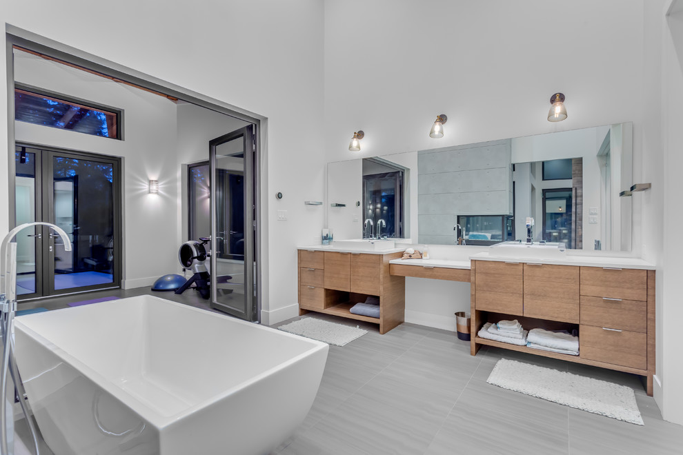 This is an example of a contemporary bathroom in Vancouver with flat-panel cabinets, medium wood cabinets, a freestanding tub, white walls and a vessel sink.