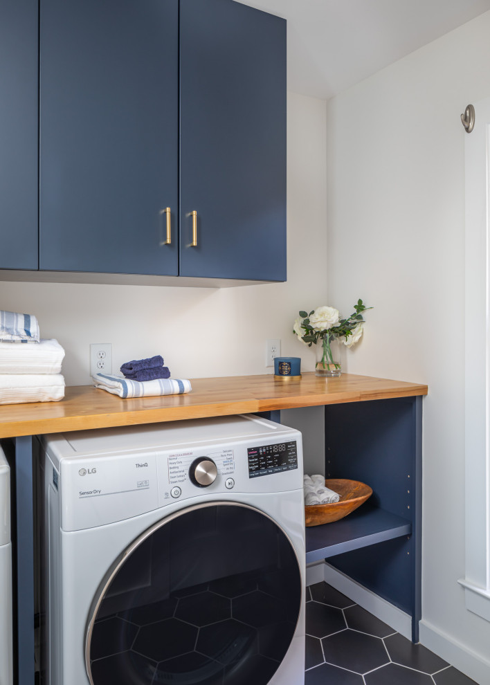 Idee per una piccola sala lavanderia contemporanea con ante lisce, ante blu, top in legno, pareti bianche, pavimento con piastrelle in ceramica, lavatrice e asciugatrice affiancate, pavimento nero e top marrone