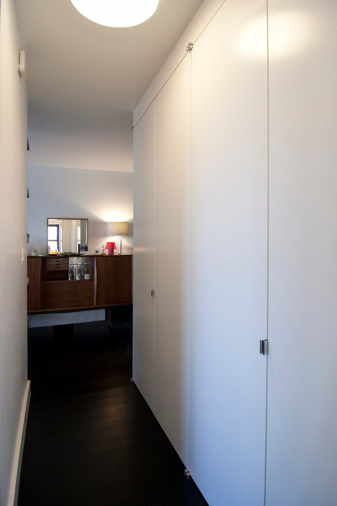 This is an example of a small midcentury hallway in New York with white walls, dark hardwood floors and black floor.