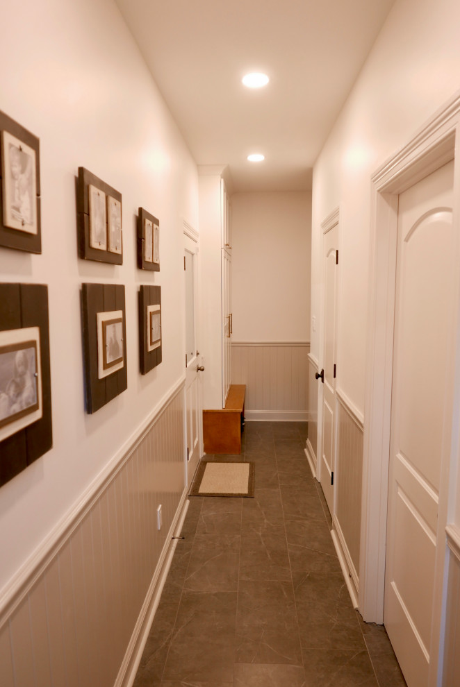 На фото: большой коридор в стиле неоклассика (современная классика) с белыми стенами, полом из керамогранита, черным полом и панелями на стенах