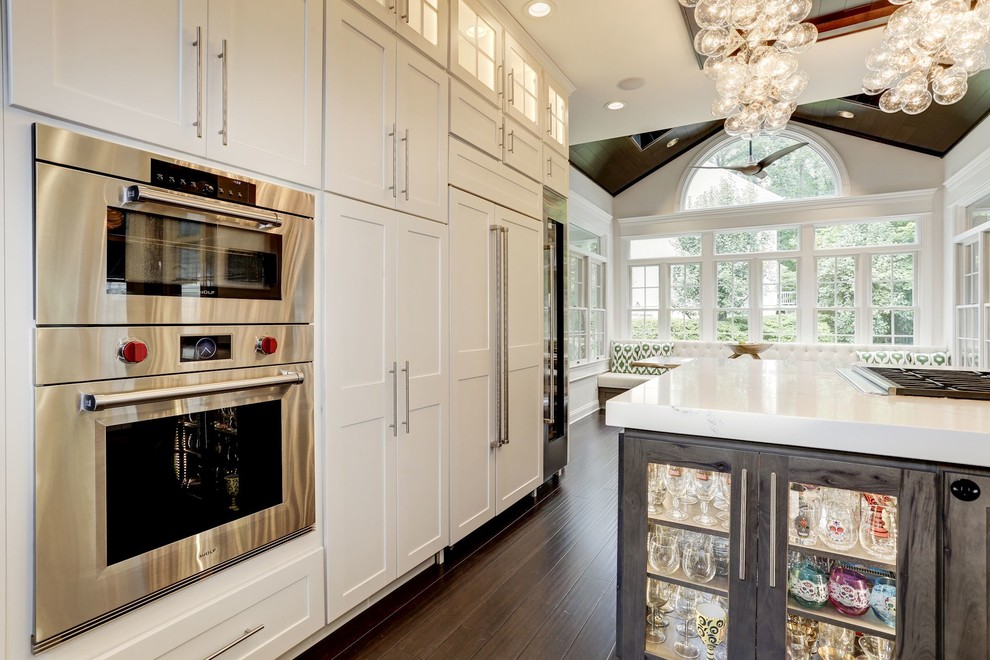 Inspiration for a mid-sized transitional u-shaped eat-in kitchen in Baltimore with an undermount sink, glass-front cabinets, white cabinets, onyx benchtops, metallic splashback, metal splashback, stainless steel appliances, dark hardwood floors, with island, brown floor and white benchtop.
