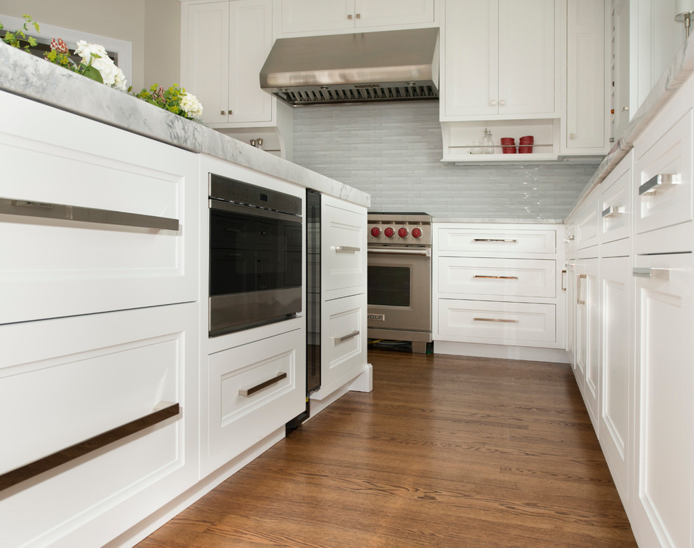 Example of a mid-sized transitional l-shaped dark wood floor eat-in kitchen design in Chicago with an undermount sink, recessed-panel cabinets, white cabinets, quartzite countertops, white backsplash, glass tile backsplash, stainless steel appliances and an island