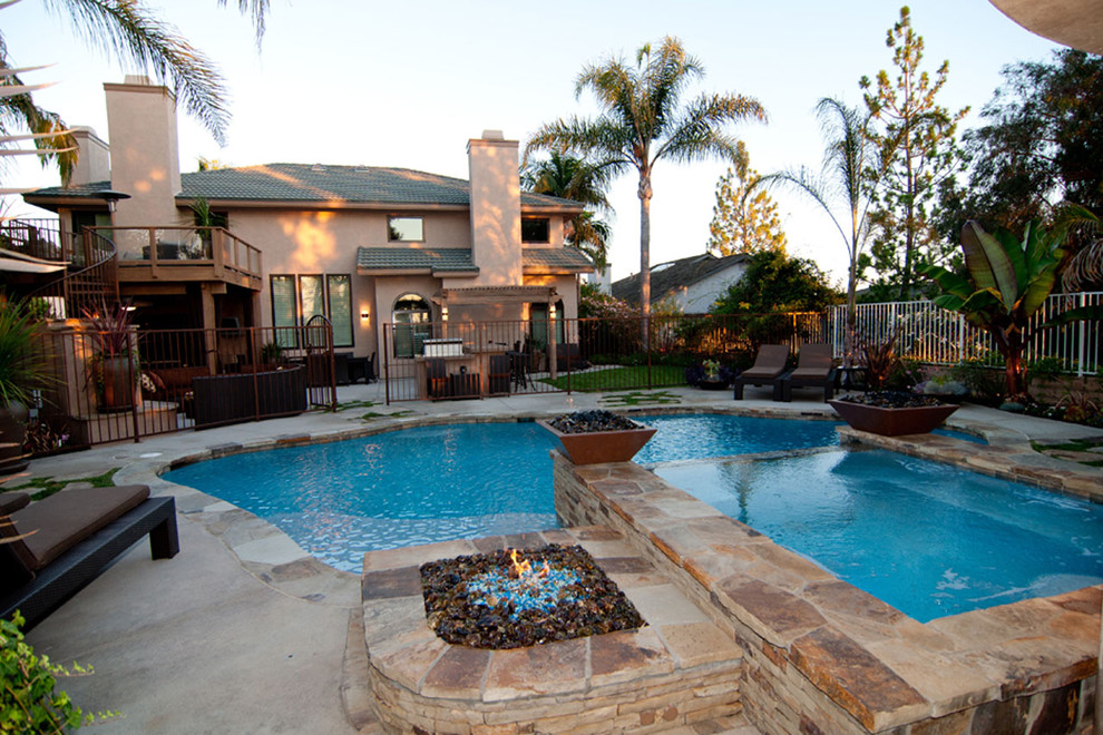 Photo of a large transitional backyard custom-shaped natural pool in Orange County with a hot tub and natural stone pavers.