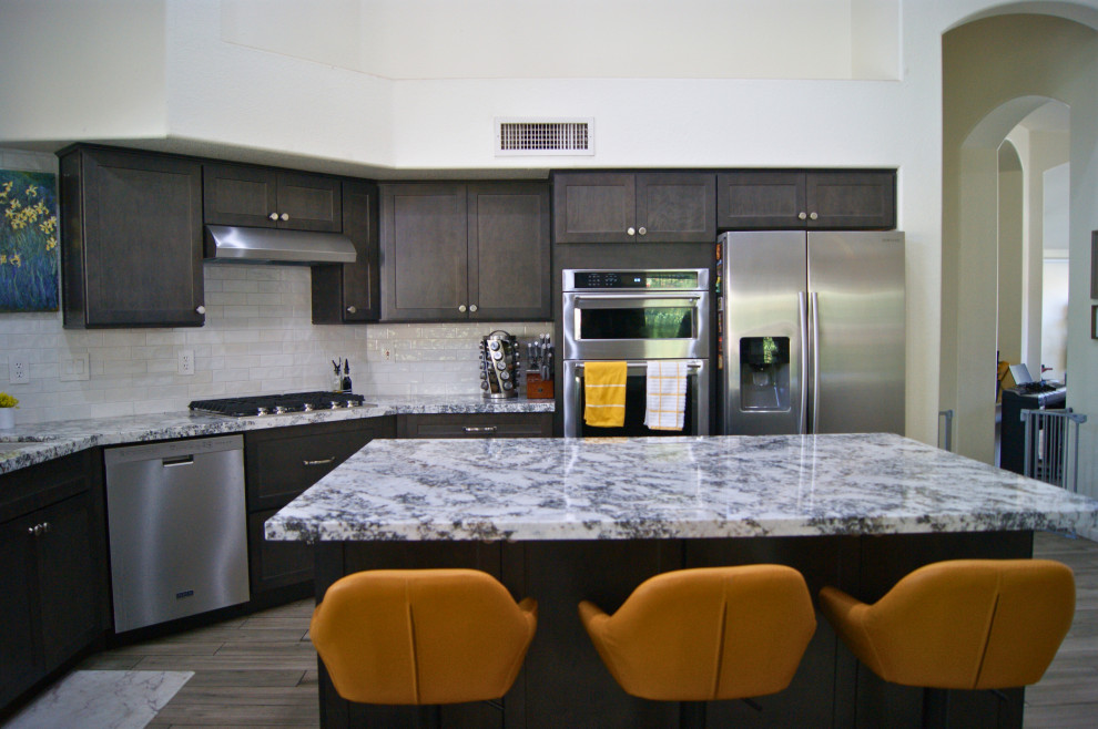 Inspiration for a mid-sized modern l-shaped porcelain tile and gray floor open concept kitchen remodel in Phoenix with an undermount sink, shaker cabinets, brown cabinets, granite countertops, white backsplash, subway tile backsplash, stainless steel appliances, an island and white countertops