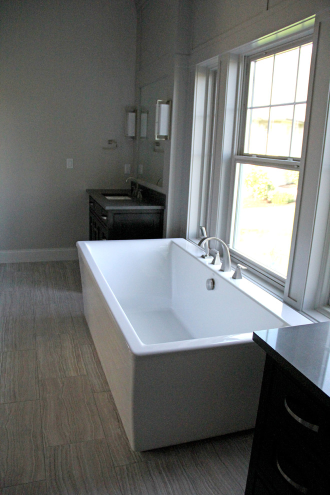Large master brown tile and porcelain tile porcelain tile and brown floor freestanding bathtub photo with flat-panel cabinets, black cabinets, gray walls, an undermount sink and granite countertops