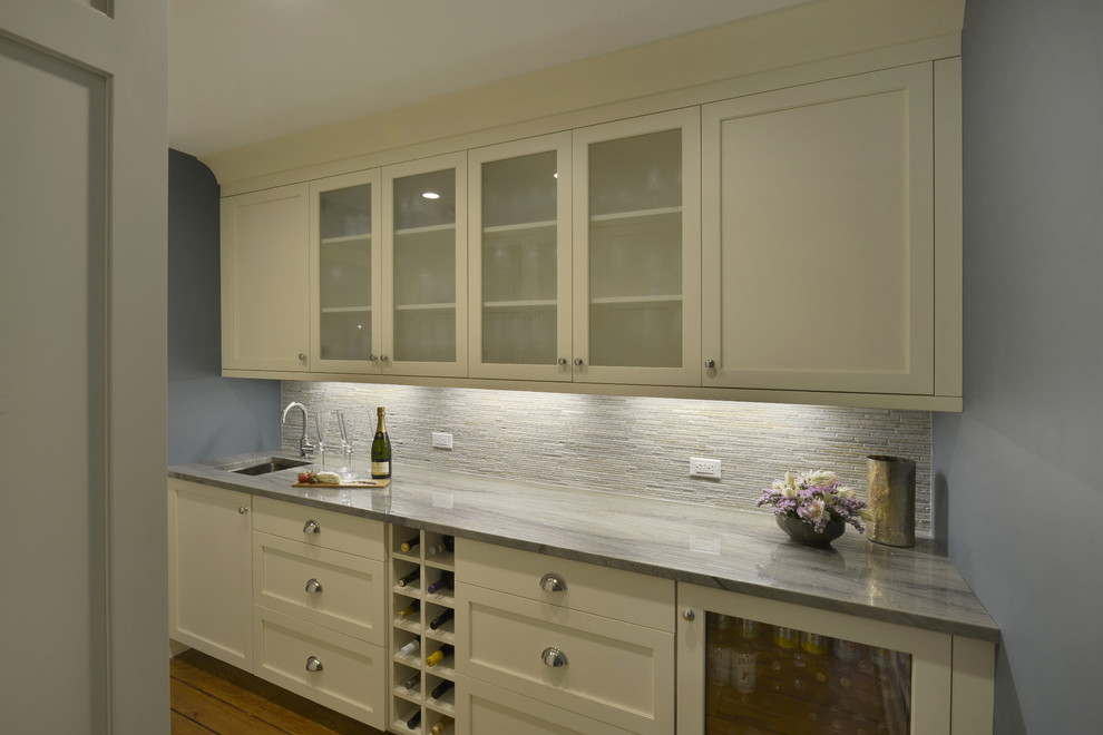 Mid-sized transitional galley wet bar in New York with an undermount sink, beaded inset cabinets, beige cabinets, quartzite benchtops, grey splashback, stone tile splashback, medium hardwood floors and brown floor.