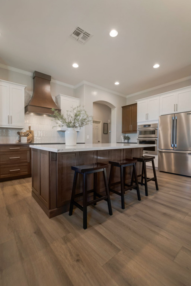 Large transitional u-shaped laminate floor and brown floor open concept kitchen photo in Phoenix with an undermount sink, shaker cabinets, medium tone wood cabinets, quartzite countertops, white backsplash, porcelain backsplash, stainless steel appliances, an island and black countertops