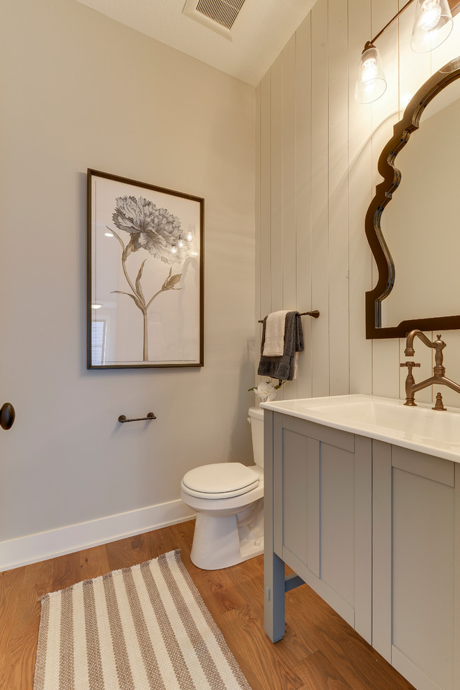 Inspiration for a small country 3/4 medium tone wood floor and brown floor bathroom remodel in Minneapolis with blue cabinets, a one-piece toilet, gray walls, solid surface countertops, shaker cabinets and an integrated sink