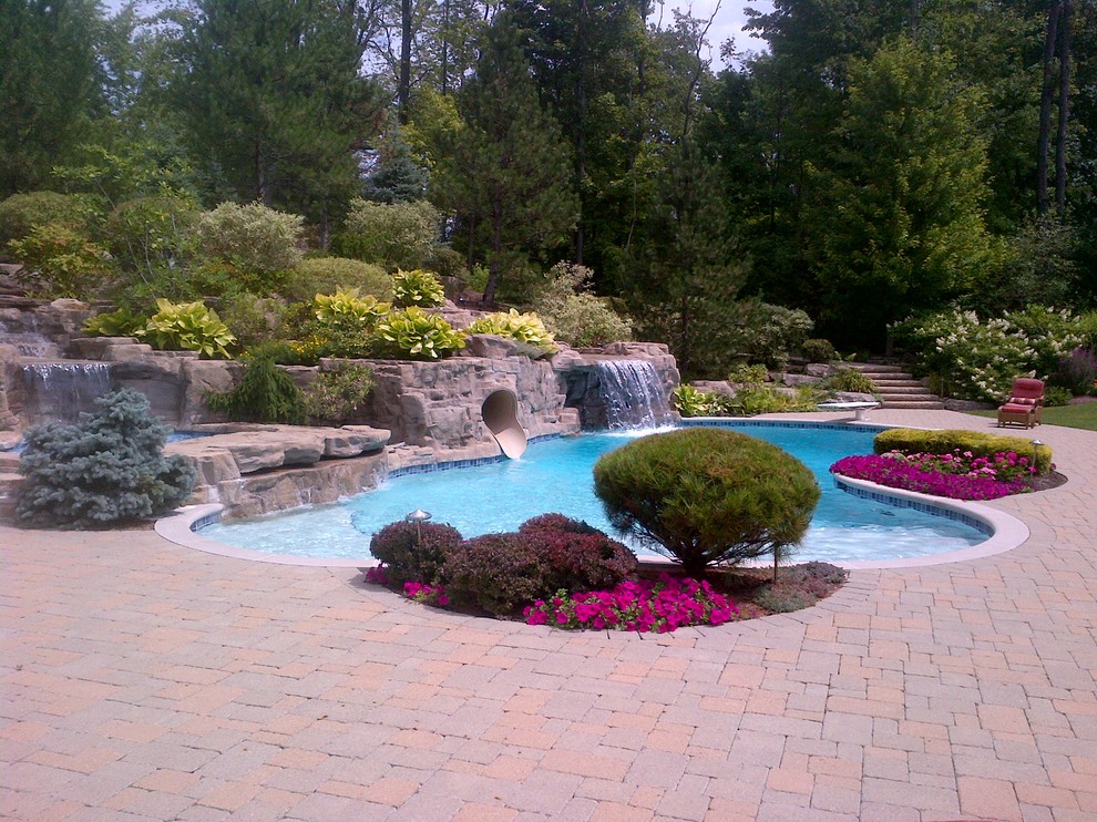 This is an example of a large contemporary backyard kidney-shaped pool in Cleveland with a water slide and brick pavers.