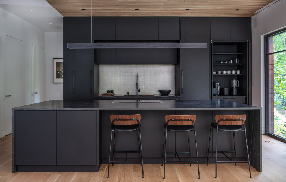 Aménagement d'une cuisine contemporaine avec une crédence métallisée, parquet clair, îlot, plan de travail noir et un plafond en bois.