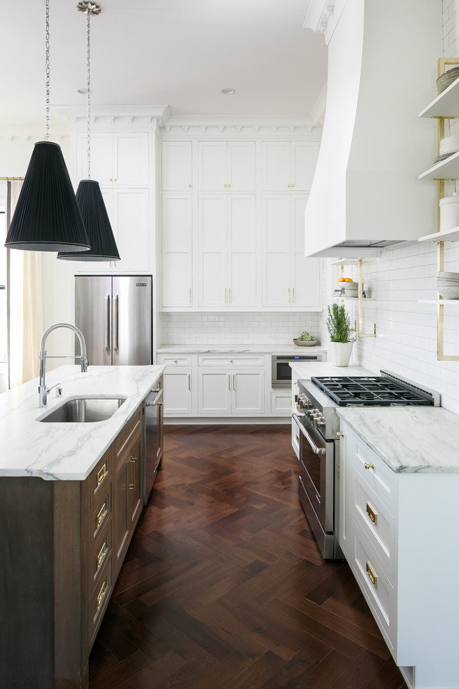 This is an example of a large transitional l-shaped open plan kitchen in Louisville with an undermount sink, beaded inset cabinets, white cabinets, marble benchtops, white splashback, subway tile splashback, stainless steel appliances, medium hardwood floors, with island and brown floor.